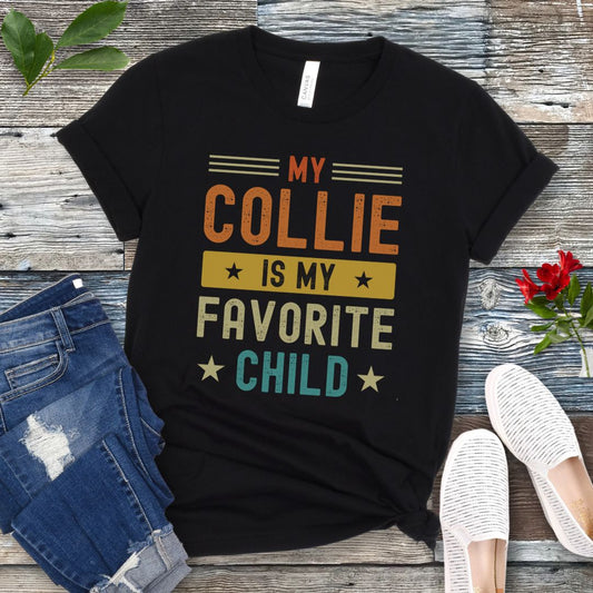 Black t-shirt for Rough Collie lovers with humorous text 'My Collie is my Favorite Child' in bold colorful retro lettering, shown on a wooden surface with jeans and shoes.