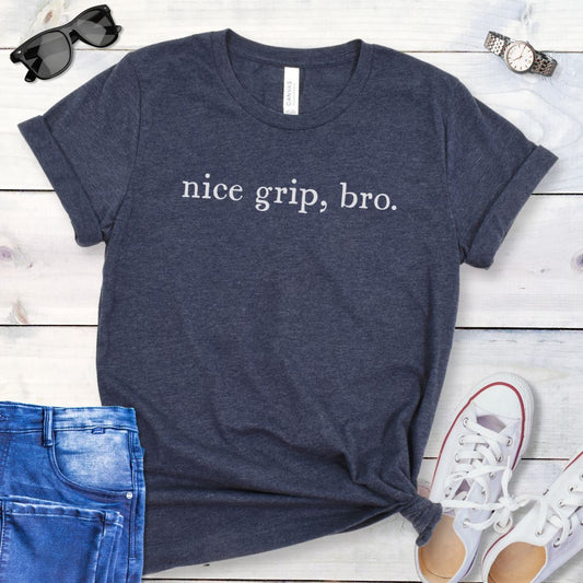 Heather navy bitework dog sport t-shirt with 'nice grip, bro.' text on a wooden surface with jeans and shoes.