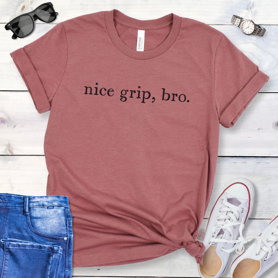 Mauve bitework dog sport t-shirt with 'nice grip, bro.' text on a wooden surface with jeans and shoes.