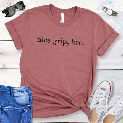 Mauve bitework dog sport t-shirt with 'nice grip, bro.' text on a wooden surface with jeans and shoes.