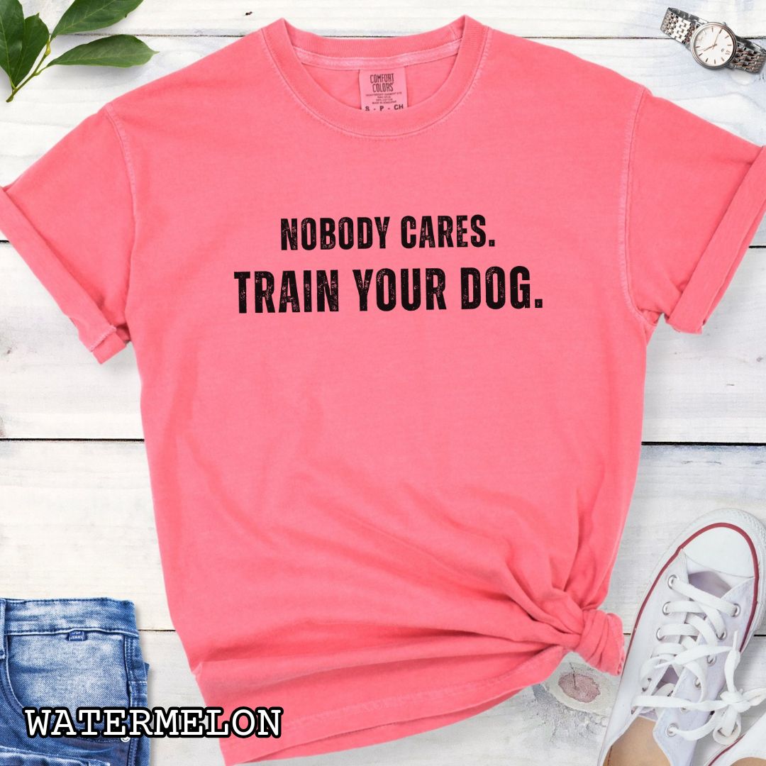 Pink Comfort Colors t-shirt featuring the phrase Nobody Cares. Train Your Dog., funny dog training shirt for dog trainers, obedience handlers, dog sports competitors, responsible dog owners, and canine training enthusiasts.