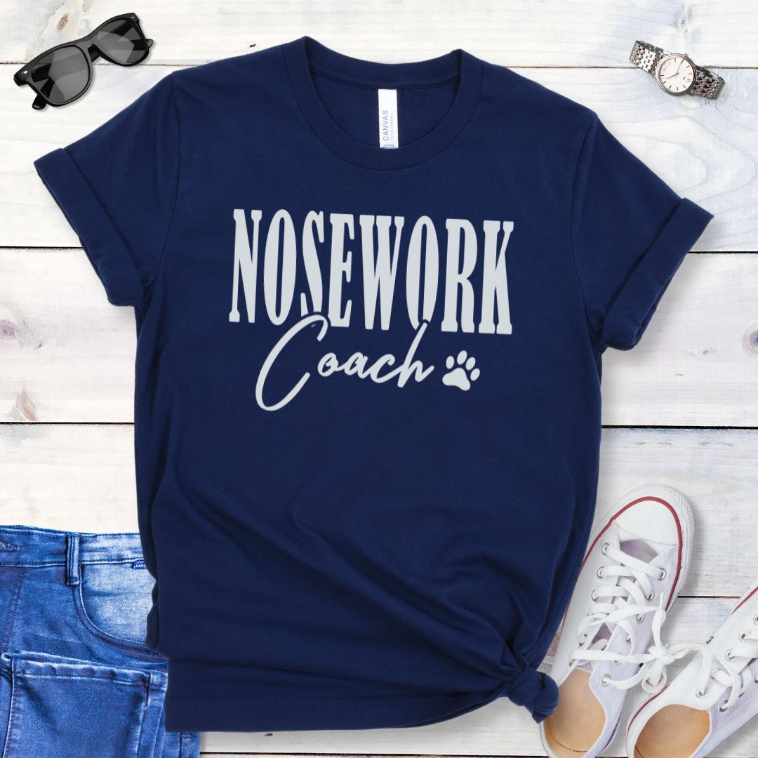 Navy blue dog trainer t-shirt with 'Nosework Coach' text, presented on a wooden surface with jeans and shoes.