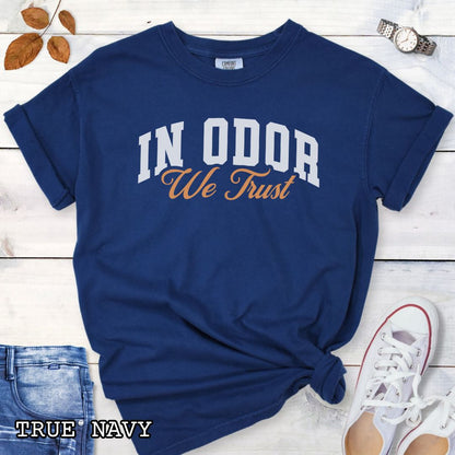 Dark blue Comfort Colors t-shirt for canine scent training enthusiasts with 'In Odor we trust' in bold athletic style lettering, shown on a wooden surface with jeans, shoes and accessories.