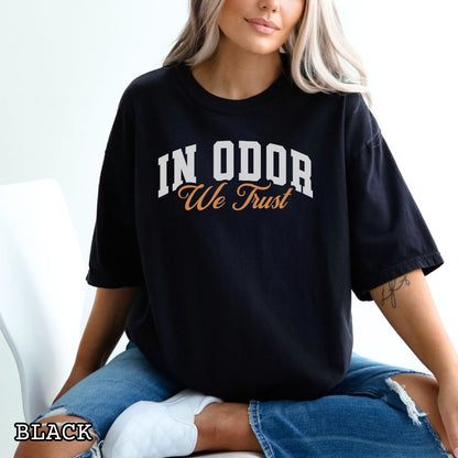 Person wearing Black Comfort Colors t-shirt for canine scent training enthusiasts with 'In Odor we trust' in bold athletic style lettering.