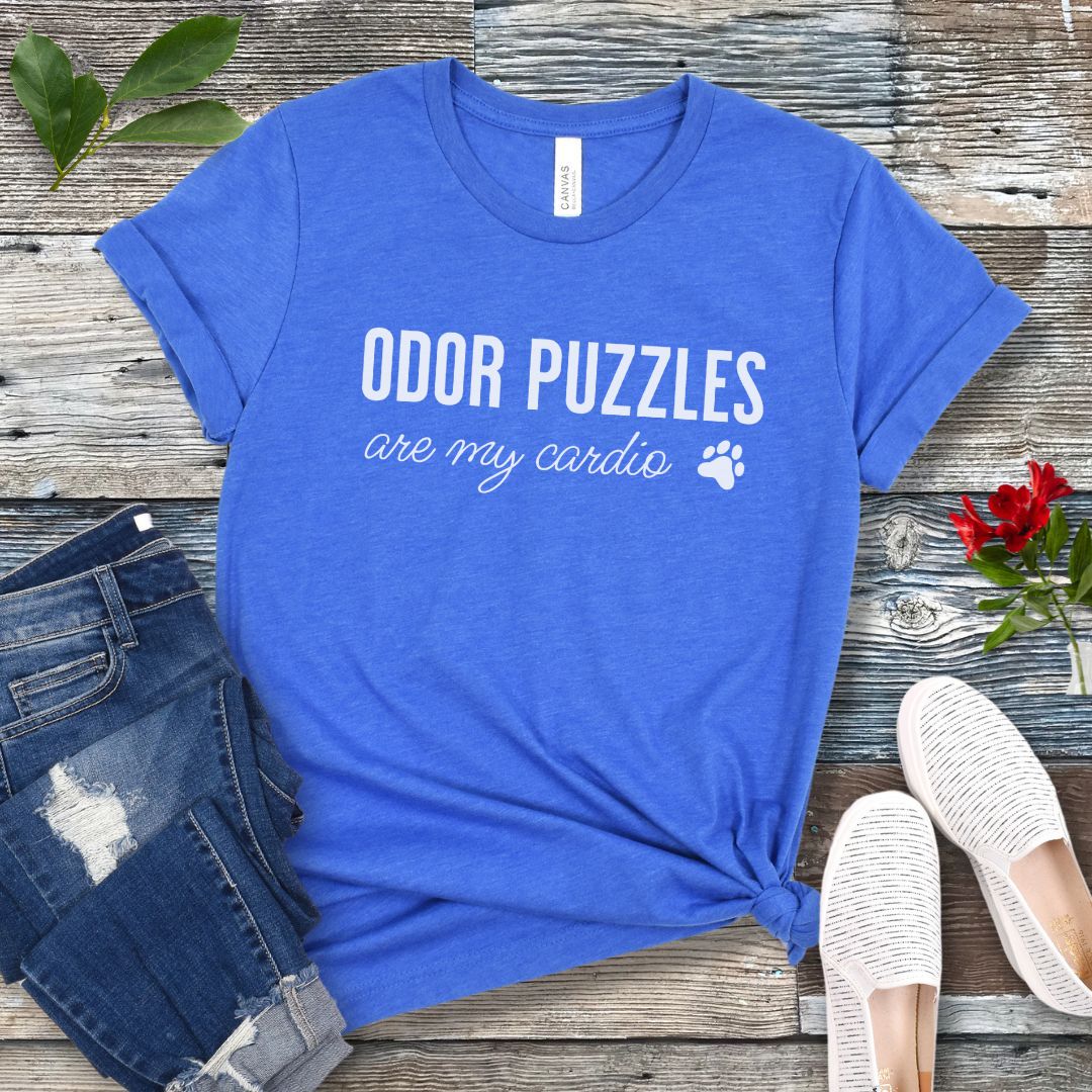 Royal blue canine scent work t-shirt with 'Odor Puzzles are my cardio' text on a wooden surface with jeans and shoes.