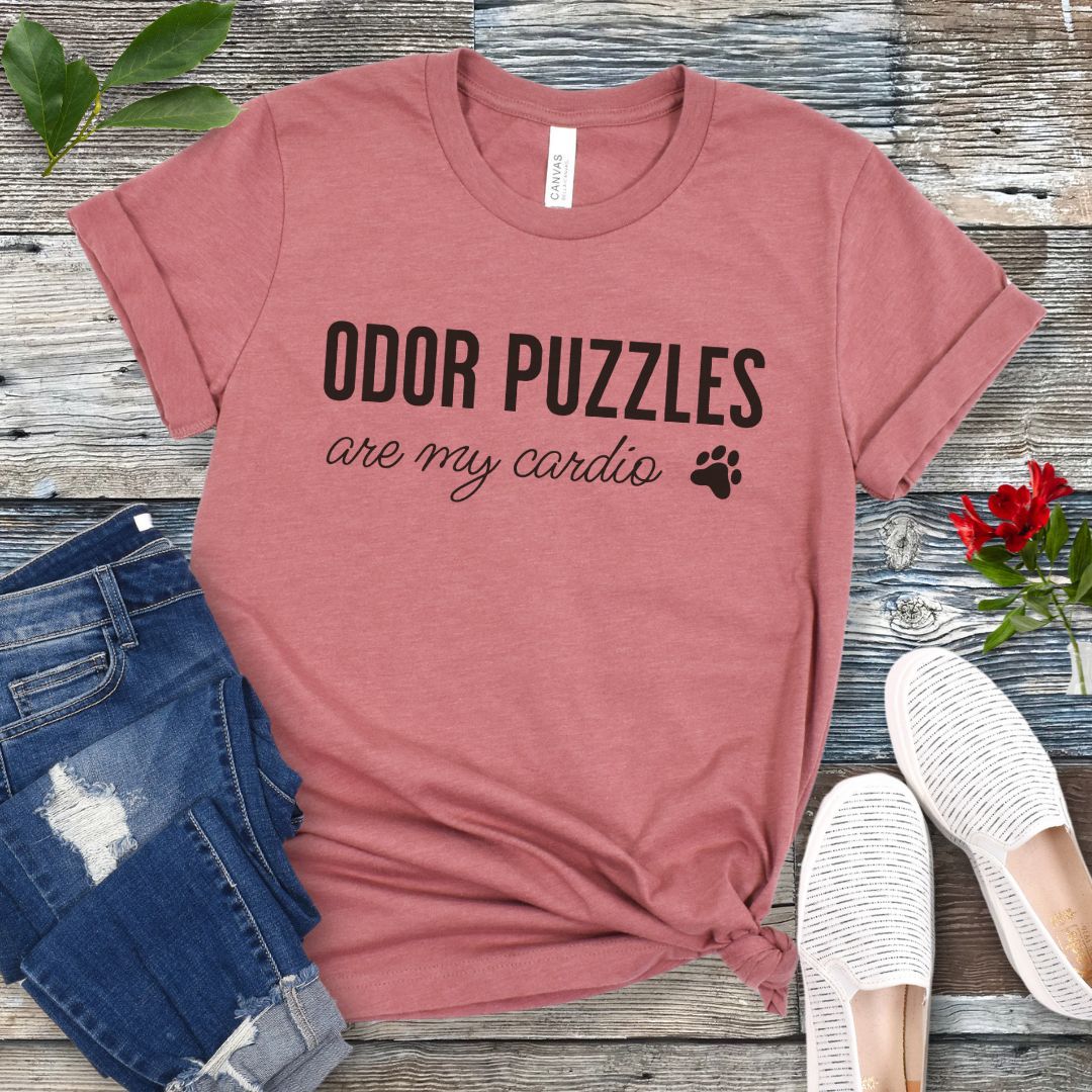 Mauve nosework for dogs t-shirt with 'Odor Puzzles are my cardio' text on a wooden surface with jeans and shoes.