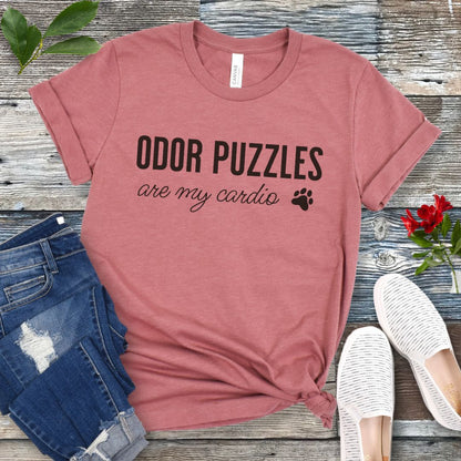 Mauve nosework for dogs t-shirt with 'Odor Puzzles are my cardio' text on a wooden surface with jeans and shoes.