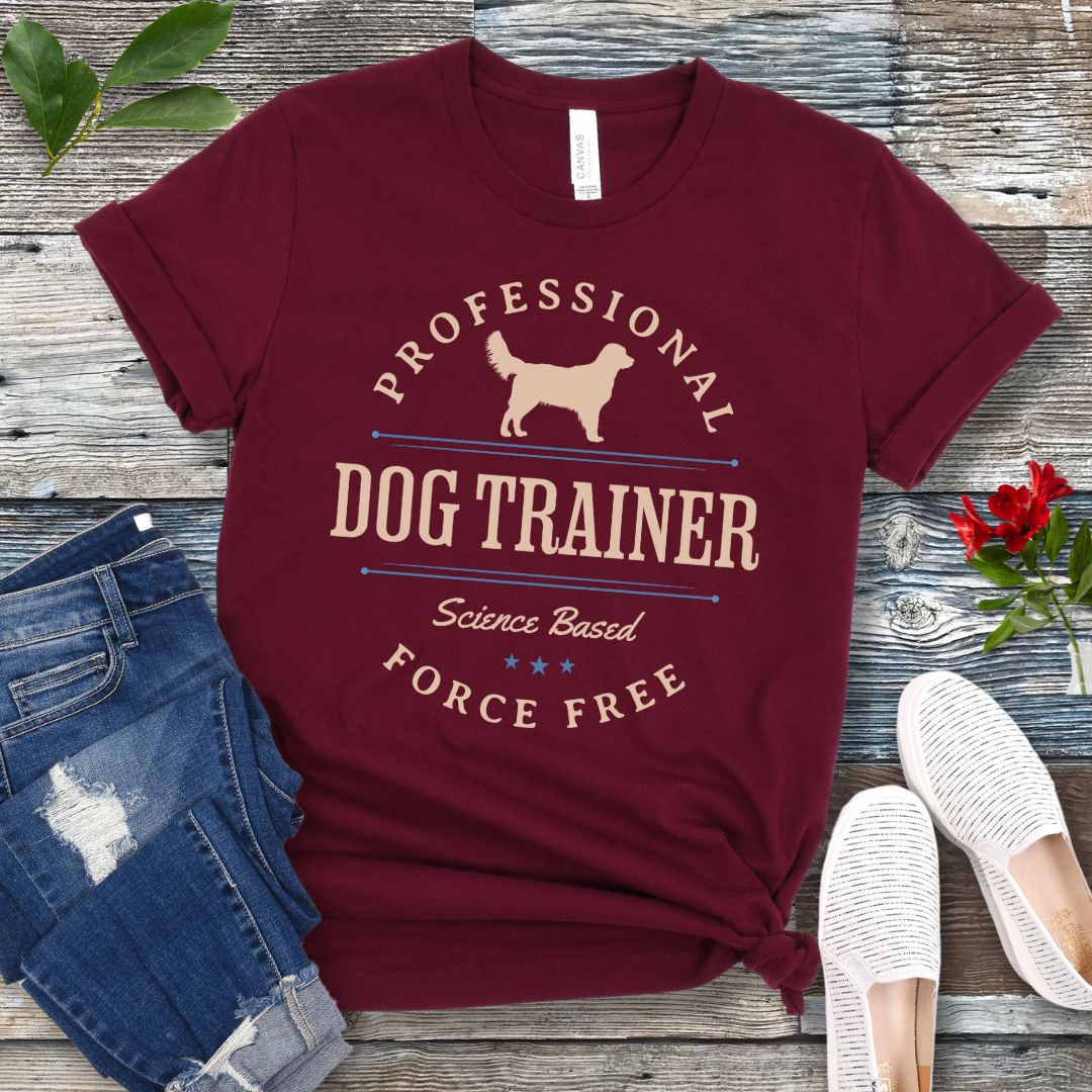 Maroon dog training t-shirt with the text 'PROFESSIONAL DOG TRAINER, Science Based, Force Free"' and custom dog breed silhouette in a vintage, badge style design. The shirt is displayed flat with a pair of blue jeans and white shoes.