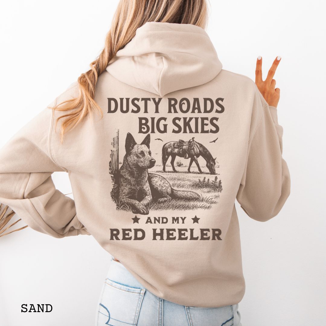 Back view of sand-beige Red Heeler hoodie featuring a Western-style design with grazing horse, rustic fence, and an Cattle Dog illustration; text reads “Dusty Roads, Big Skies, and My Red Heeler.”