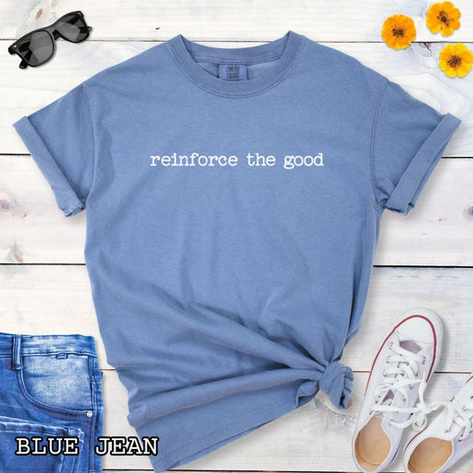 Blue (Blue Jean) Comfort Colors dog training t-shirt with 'reinforce the good' text on a wooden surface with jeans and sneakers.