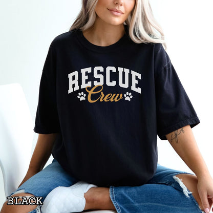 A woman wearing a black oversized graphic T-shirt with 'RESCUE Crew' printed in white and gold, paired with ripped blue jeans. The image includes a 'BLACK' color label overlay in the bottom-left corner.