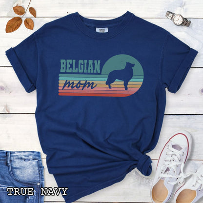 Navy blue Comfort Colors t-shirt for Belgian Sheepdog lovers with retro stripe design, Belgian silhouette and 'Belgian Mom' text, shown on a wooden surface with jeans and shoes.