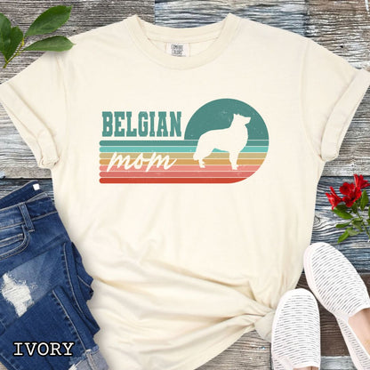 Beige Comfort Colors t-shirt for Belgian Sheepdog lovers with retro stripe design, Belgian silhouette and 'Belgian Mom' text, shown on a wooden surface with jeans and shoes.