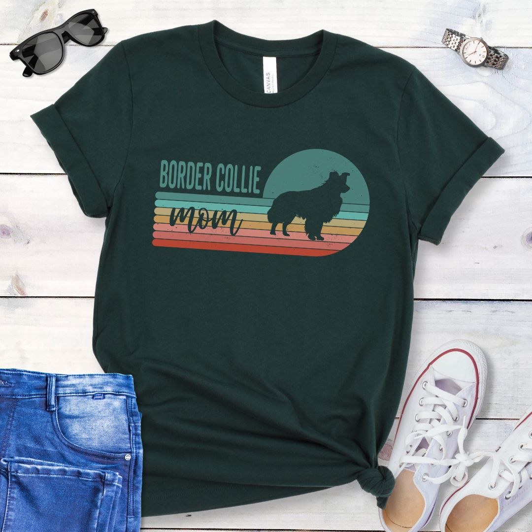 Dark green t-shirt with retro style 'Border Collie Mom' design on a wooden surface with jeans and shoes.