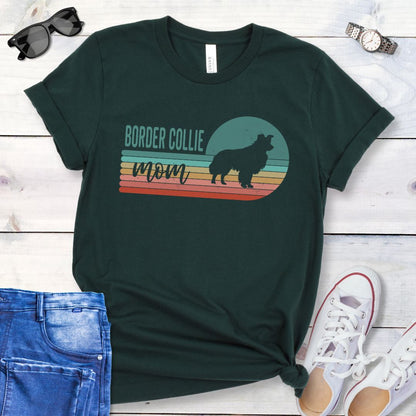 Dark green t-shirt with retro style 'Border Collie Mom' design on a wooden surface with jeans and shoes.