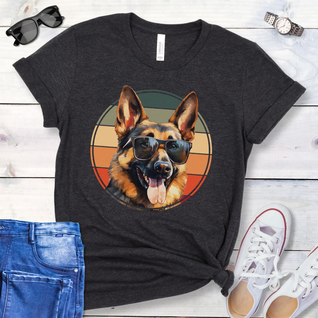 Dark grey t-shirt for German Shepherd lovers with smiling Shepherd dog wearing sunglasses and vintage sunset graphic, shown on a wooden surface with jeans and sneakers.