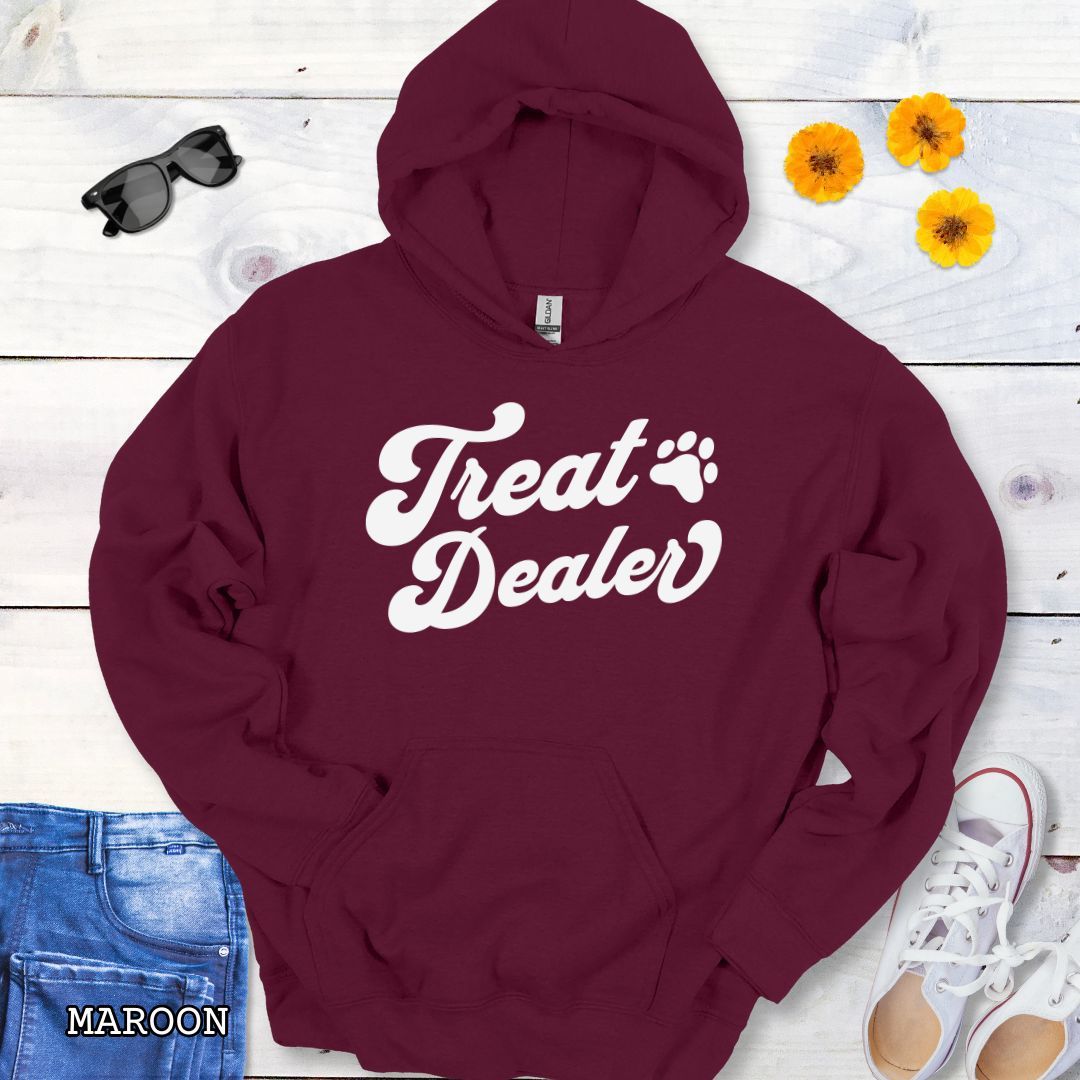 Maroon hoodie with the text 'Treat Dealer' printed on the front in retro font, accompanied by a paw print. The shirt is displayed on a wooden background with a pair of jeans and white shoes.