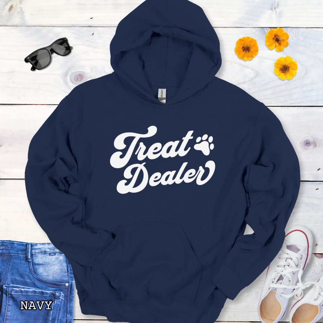 Navy hoodie with the text 'Treat Dealer' printed on the front in retro font, accompanied by a paw print. The shirt is displayed on a wooden background with a pair of jeans and white shoes.