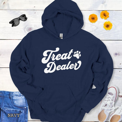 Navy hoodie with the text 'Treat Dealer' printed on the front in retro font, accompanied by a paw print. The shirt is displayed on a wooden background with a pair of jeans and white shoes.