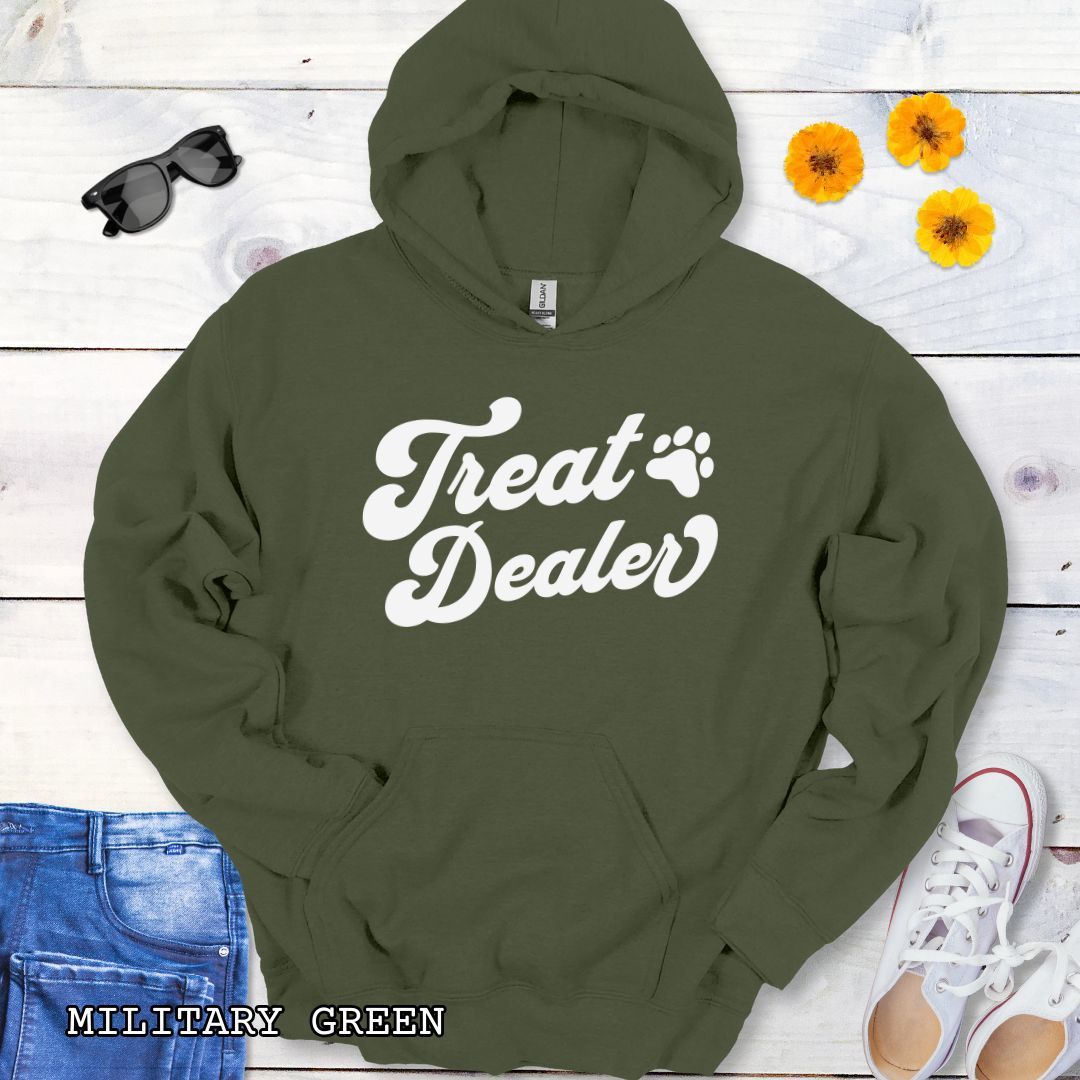 Military green hoodie with the text 'Treat Dealer' printed on the front in retro font, accompanied by a paw print. The shirt is displayed on a wooden background with a pair of jeans and white shoes.