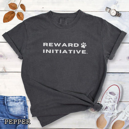 Dark grey Pepper) Comfort Colors dog training t-shirt with 'REWARD INITIATIVE' text, presented on a wooden surface with jeans, sneakers, and sunglasses.
