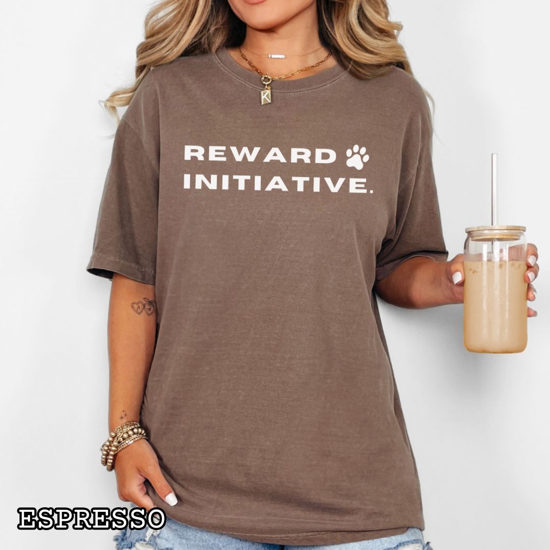 Brown (Espresso) Comfort Colors dog training t-shirt with 'REWARD INITIATIVE' text, presented on a wooden surface with jeans, sneakers, and sunglasses.