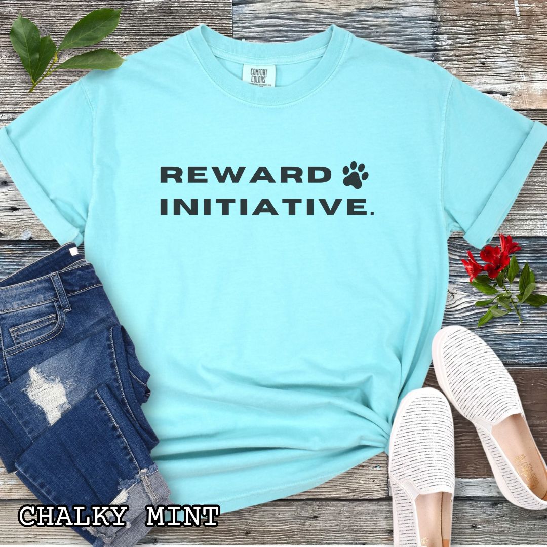Green (Chalky Mint) Comfort Colors dog training t-shirt with 'REWARD INITIATIVE' text, presented on a wooden surface with jeans, sneakers, and sunglasses.