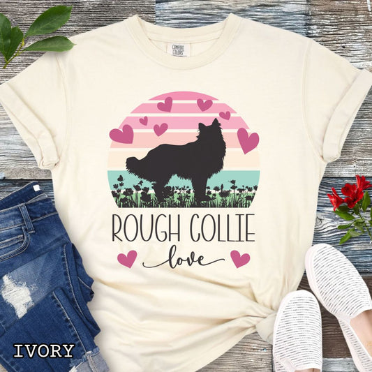 Beige Comfort Colors t-shirt with colorful vintage sunset design with hearts, flowers, and Rough Collie silhouette and the text 'Rough Collie Love', shown on a wooden surface.