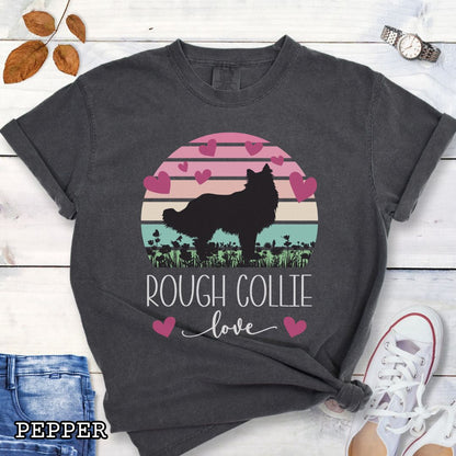 Dark grey Comfort Colors t-shirt with colorful vintage sunset design with hearts, flowers, and Rough Collie silhouette and the text 'Rough Collie Love', shown on a wooden surface.