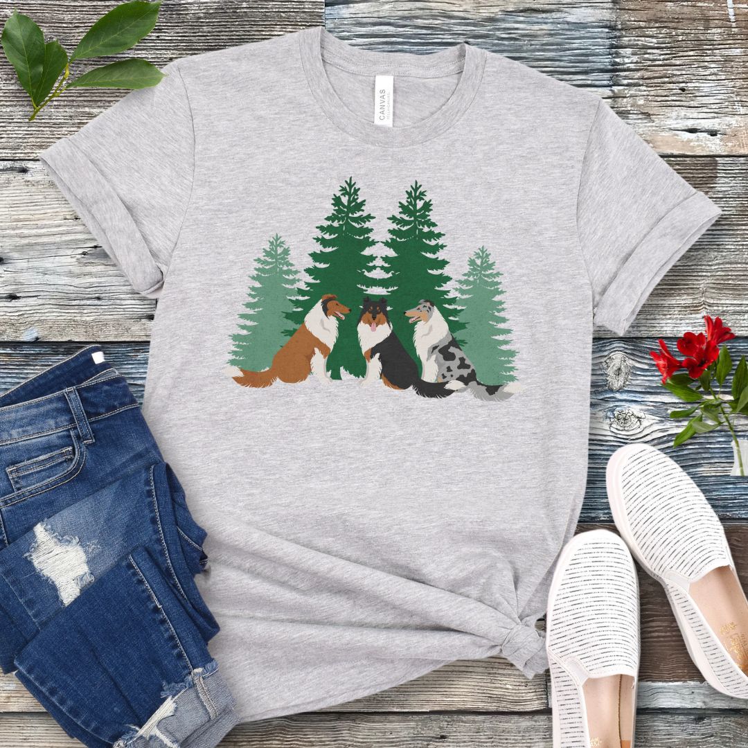 Grey Collie lover t-shirt with tricolor, sable and white and blue merle Rough Collies sitting in front of evergreen trees, shown on a wooden surface with jeans and shoes.