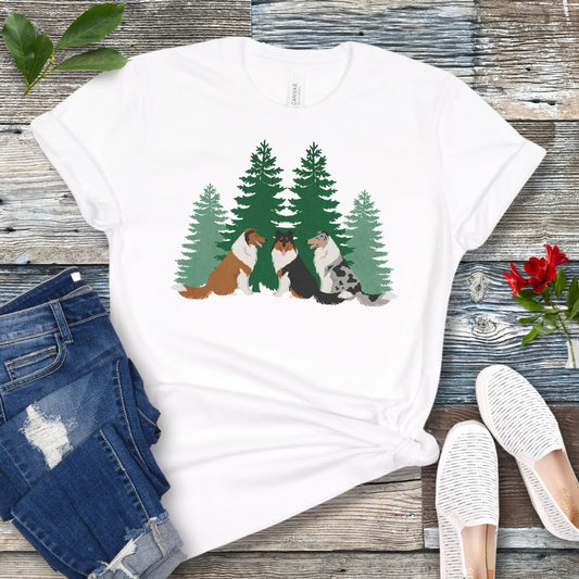 White Collie lover t-shirt with tricolor, sable and white and blue merle Rough Collies sitting in front of evergreen trees, shown on a wooden surface with jeans and shoes.