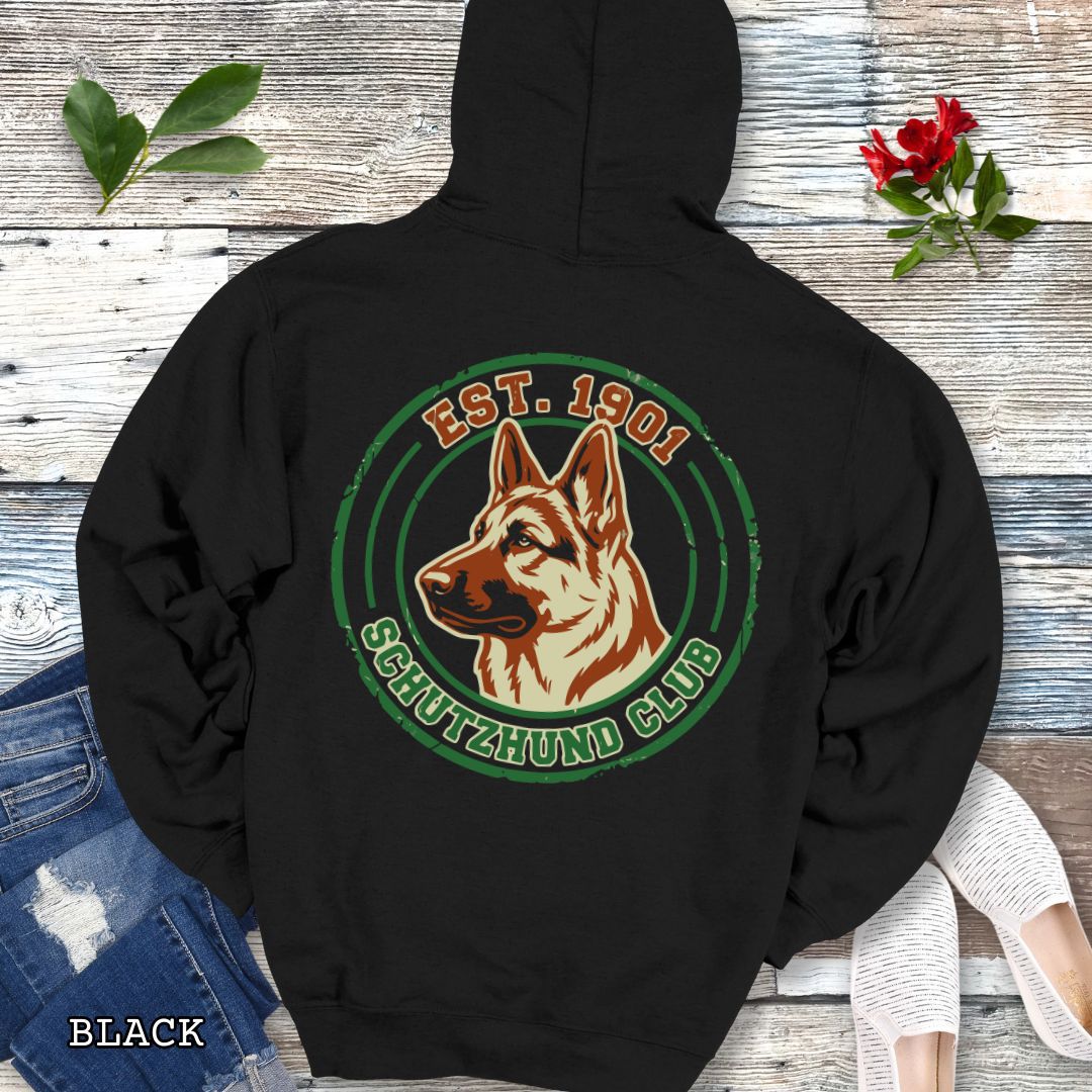 Black back print hoodie with a  German Shepherd Dog and 'Established 1901, Schutzhund Club' text in a circular logo style design, displayed on a wooden surface with flowers and jeans.