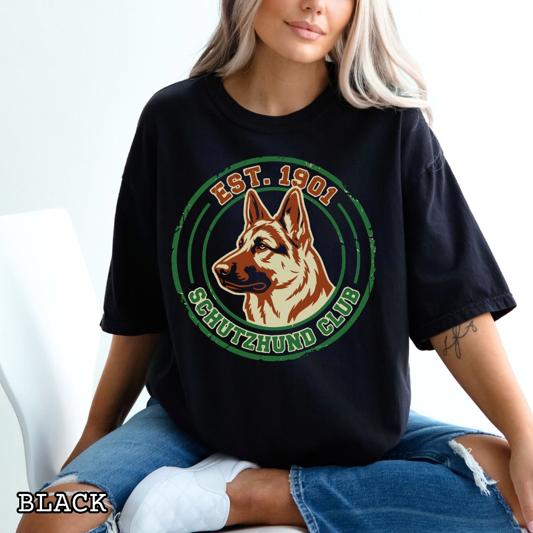 Person wearing a black Comfort Colors t-shirt with a Schutzhund Club logo featuring a German Shepherd.
