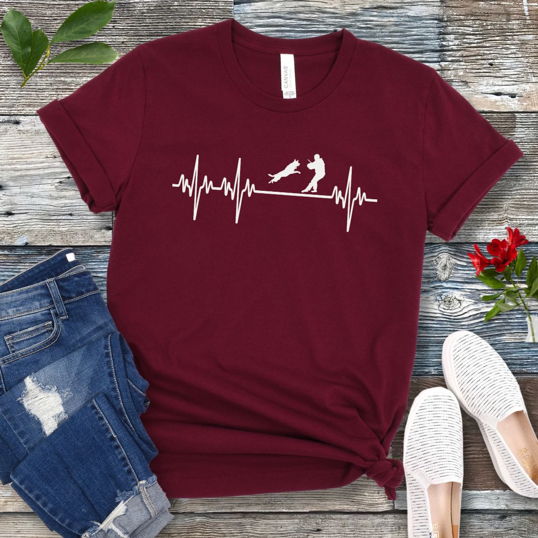 Maroon bitework t-shirt with an EKG graphic and protection dog design on a wooden surface with jeans and shoes.