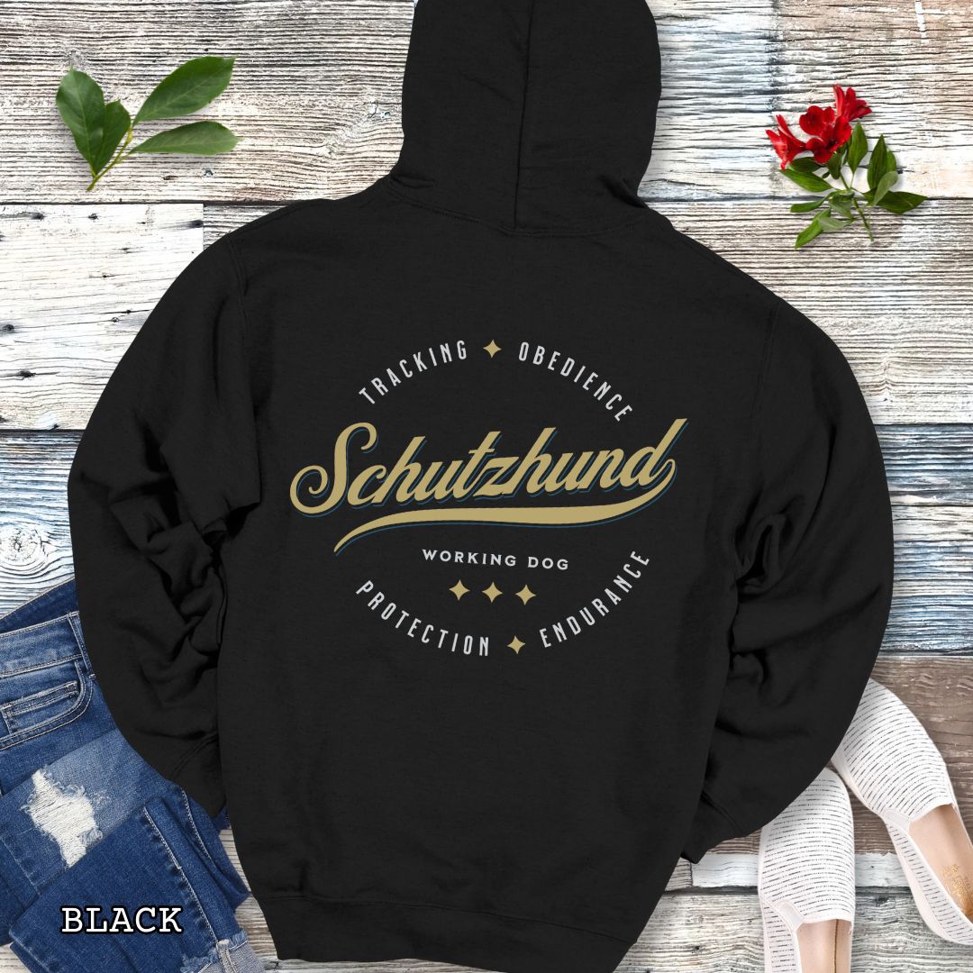 Back view of a black unisex Schutzhund/IGP hoodie with vintage style text design that reads 'Schutzhund, Working Dog, Tracking, Obedience, Protection, Endurance'. Presented on a wooden background with jeans and shoes.