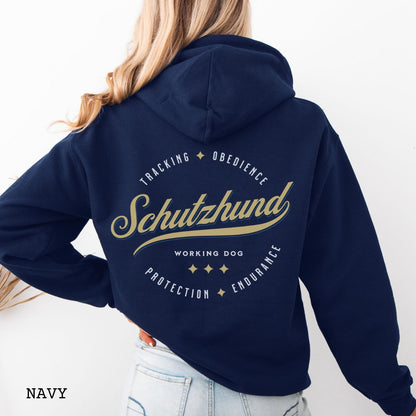 Back view of a navy blue unisex Schutzhund/IGP hoodie with vintage style text design that reads 'Schutzhund, Working Dog, Tracking, Obedience, Protection, Endurance'. Presented on a wooden background with jeans and shoes.