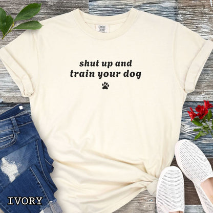 Beige Comfort Colors t-shirt featuring the phrase Shut Up and Train Your Dog with paw print graphic, funny dog training shirt for dog trainers, obedience handlers, canine training enthusiasts, and dog sports competitors.