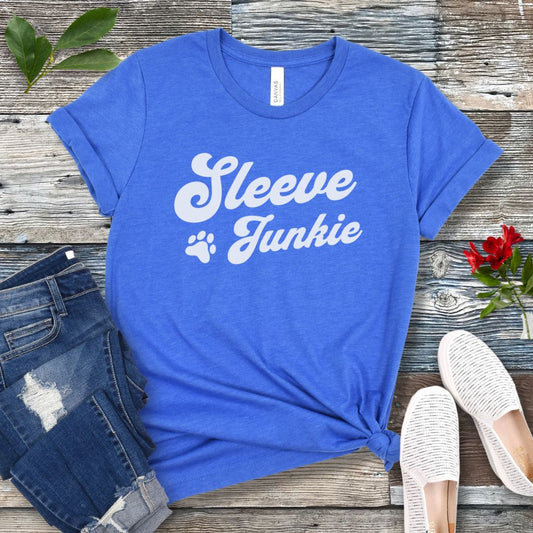 Royal blue IGP bite work t-shirt with 'Sleeve Junkie' text bold, retro font and paw print on a wooden surface with jeans and shoes.