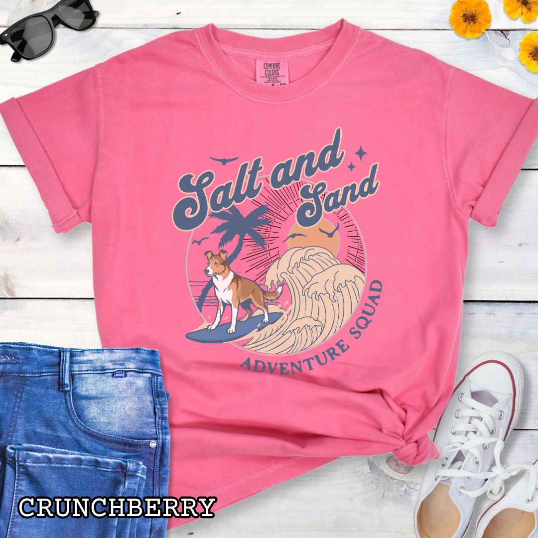 Bright pink Comfort Colors t-shirt for Smooth Collie lovers with retro surfing Smooth Collie dog graphic in a beach setting with 'Salt and Sand Adventure Squad' text, shown on a wooden surface.
