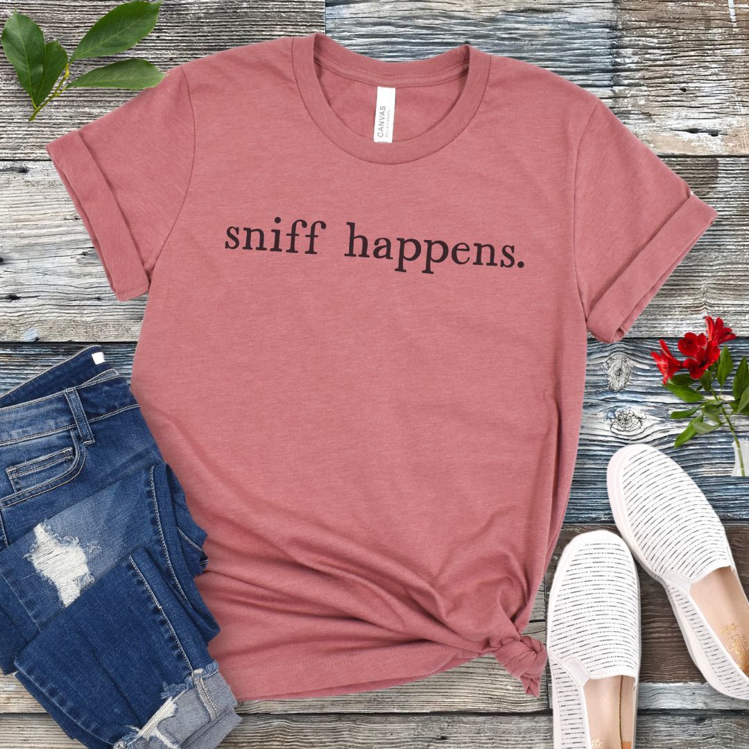Mauve K9 nosework t-shirt with 'sniff happens.' text on a wooden surface with jeans and shoes.