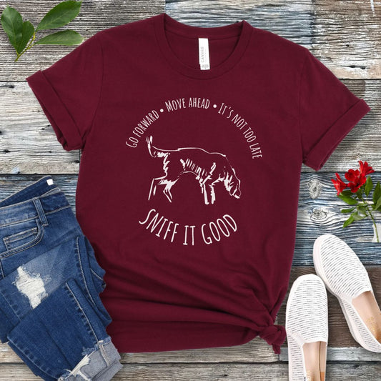 Maroon scent work t-shirt with a graphic print of a dog sniffing and text that reads 'Sniff it good'. The t-shirt is presented flat with casual clothing and shoes.