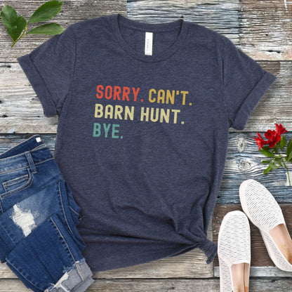 Heather navy dog sports t-shirt with colorful text 'SORRY. CAN'T. BARN HUNT. BYE.' on a wooden surface with jeans and shoes.