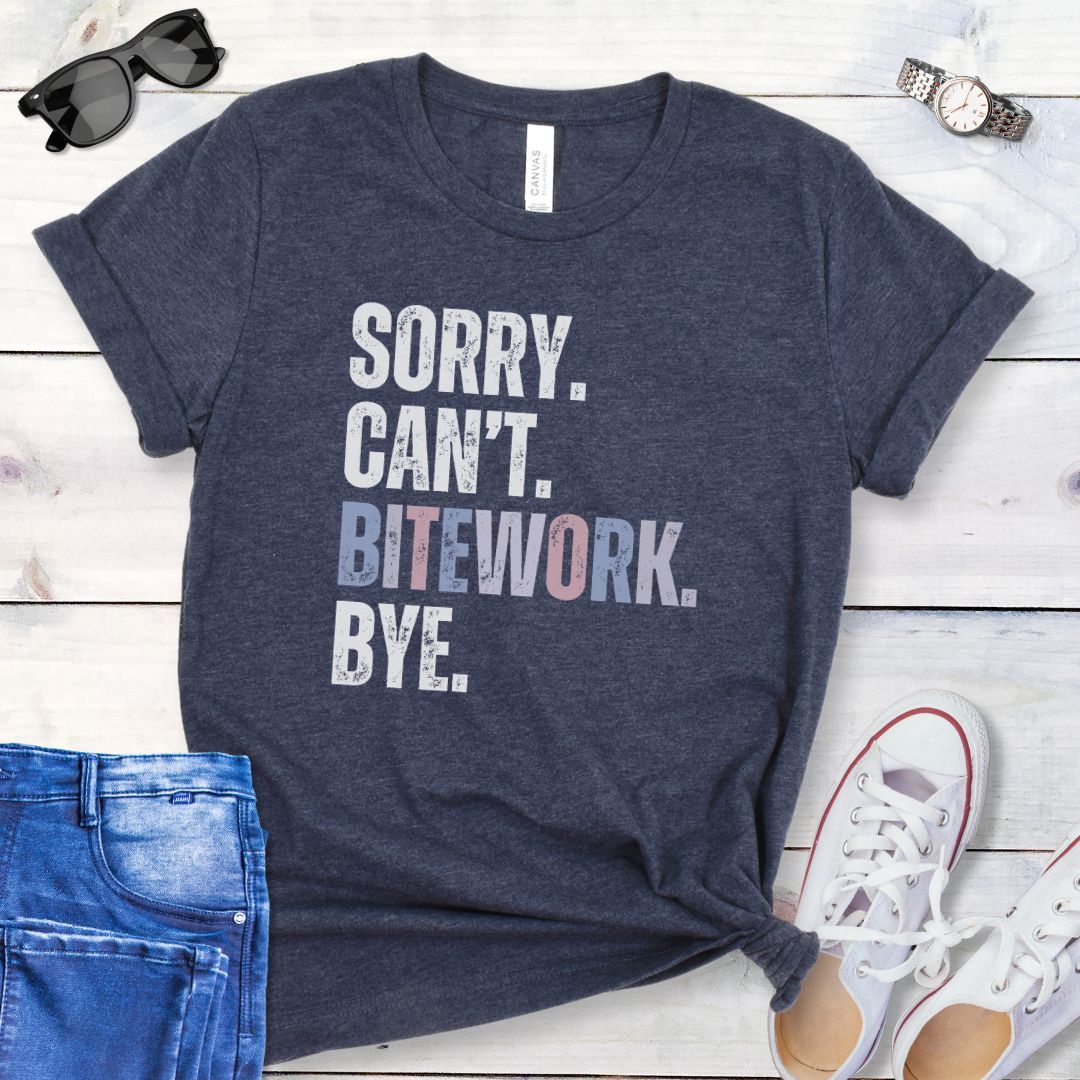Heather navy protection dog training t-shirt with colorful, distressed text 'SORRY. CAN'T. BITEWORK. BYE.', presented on a wooden surface with jeans and shoes.