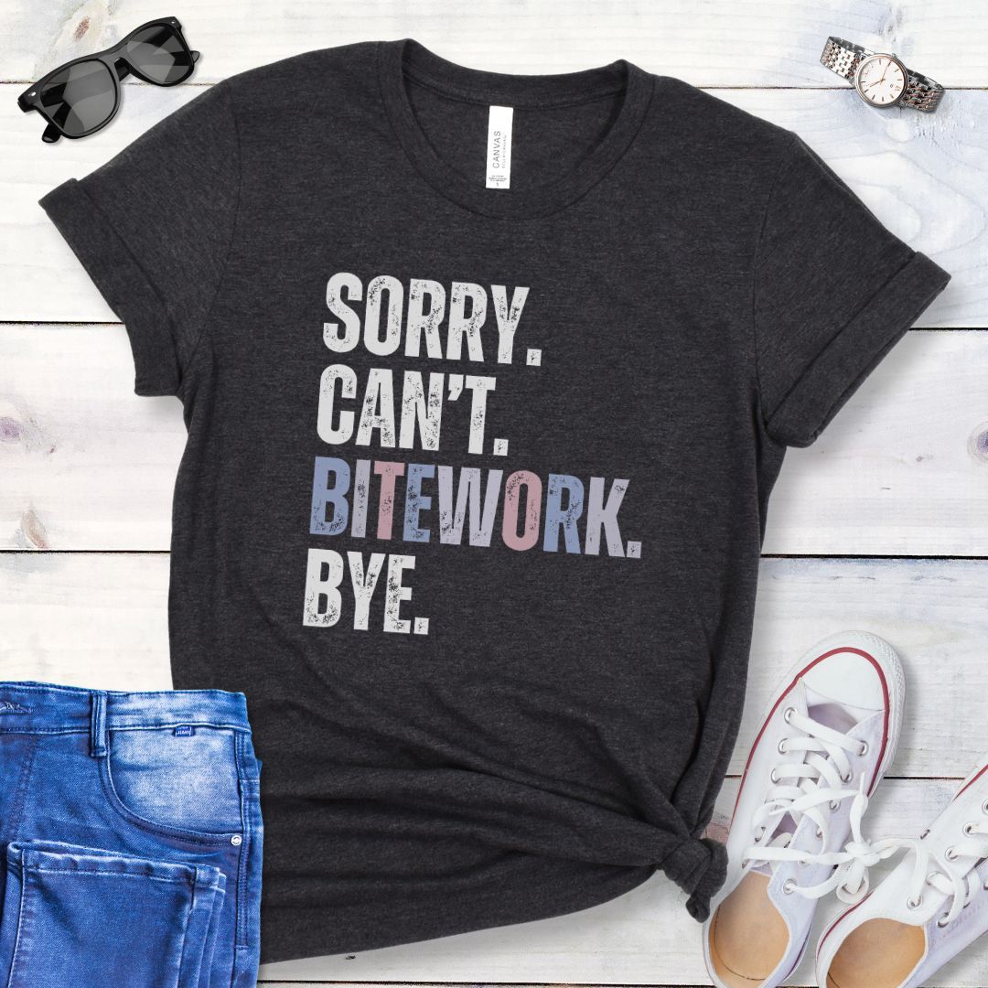 Dark grey protection dog training t-shirt with colorful, distressed text 'SORRY. CAN'T. BITEWORK. BYE.', presented on a wooden surface with jeans and shoes.