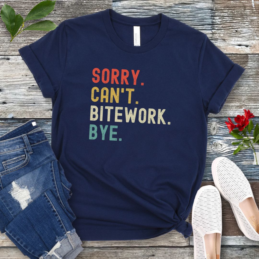 Navy blue protection dog t-shirt with bold colorful text 'SORRY. CAN'T. BITEWORK. BYE.', presented on a wooden surface with jeans and shoes.