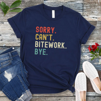 Navy blue protection dog t-shirt with bold colorful text 'SORRY. CAN'T. BITEWORK. BYE.', presented on a wooden surface with jeans and shoes.