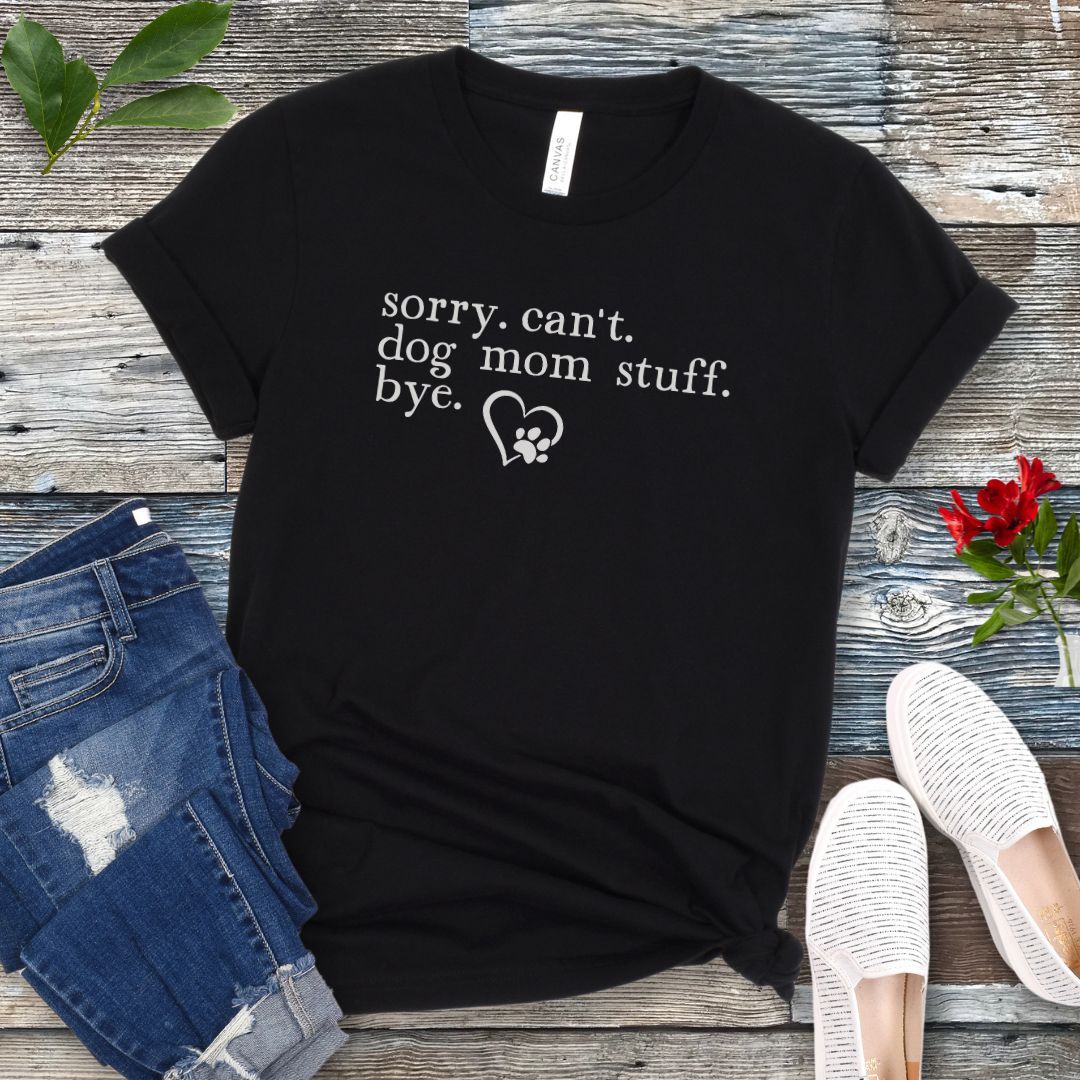 A black dog lover t-shirt with the text 'sorry, can't dog mom stuff, bye' and a paw-heart detail, displayed flat with a pair of blue jeans and white sneakers.