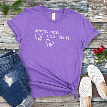 A purple dog lover t-shirt with the text 'sorry, can't dog mom stuff, bye' and a paw-heart detail, displayed flat with a pair of blue jeans and white sneakers.