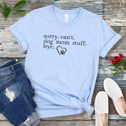 A light blue dog lover t-shirt with the text 'sorry, can't dog mom stuff, bye' and a paw-heart detail, displayed flat with a pair of blue jeans and white sneakers.