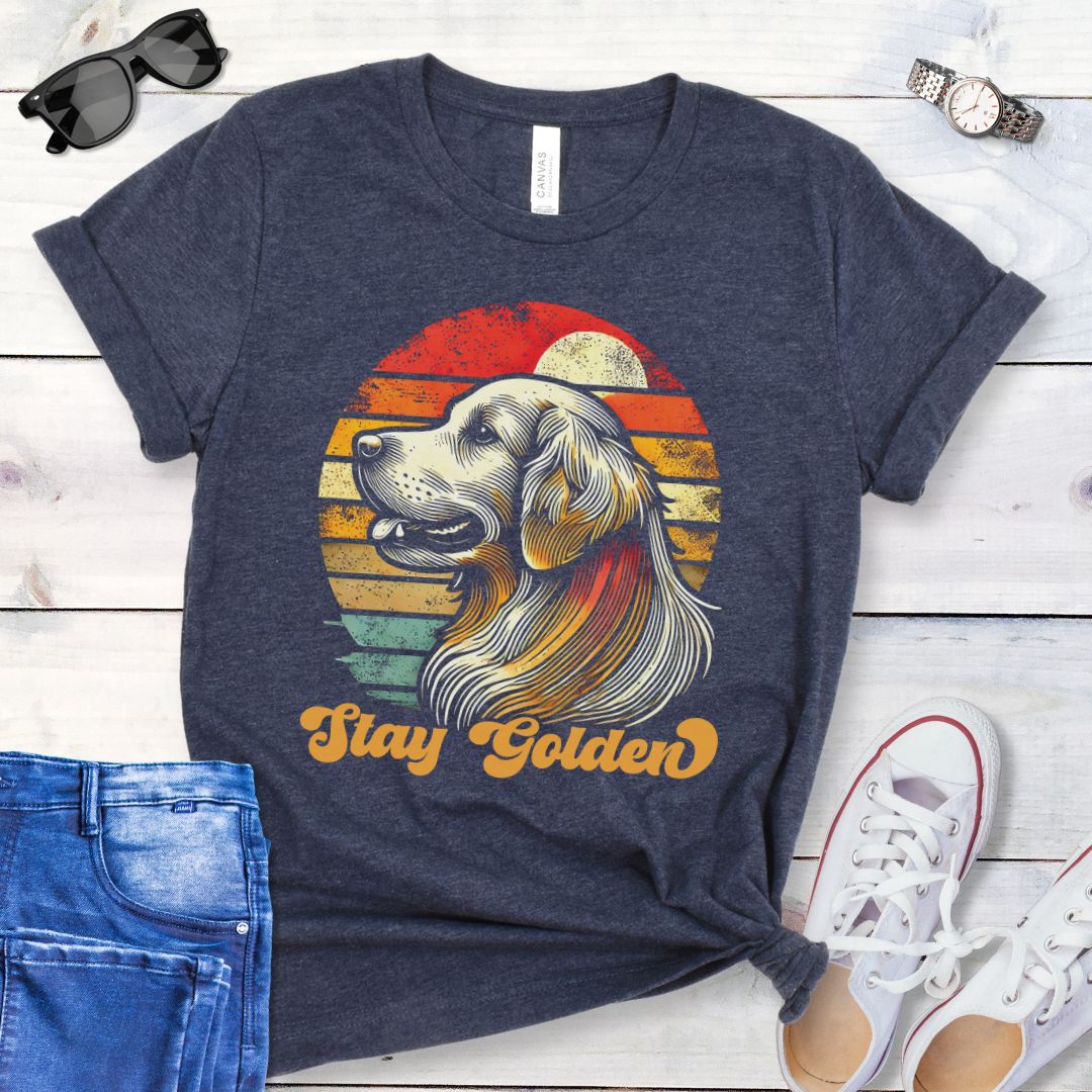 Heather navy t-shirt with 'Stay Golden' text and a vintage sunset graphic with a line drawn Golden Retriever, presented on a wooden surface with jeans and shoes.